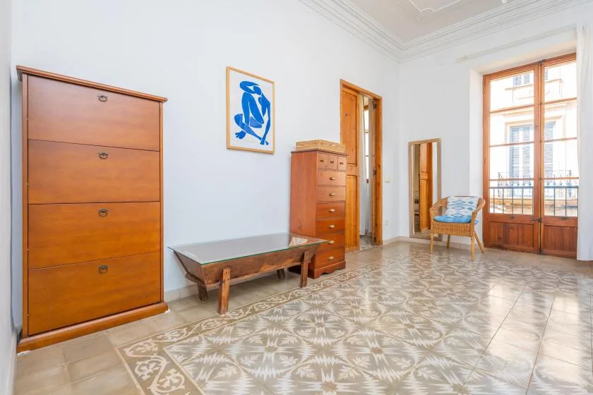 A bright room with wooden furniture, patterned tile flooring, and a large window.
