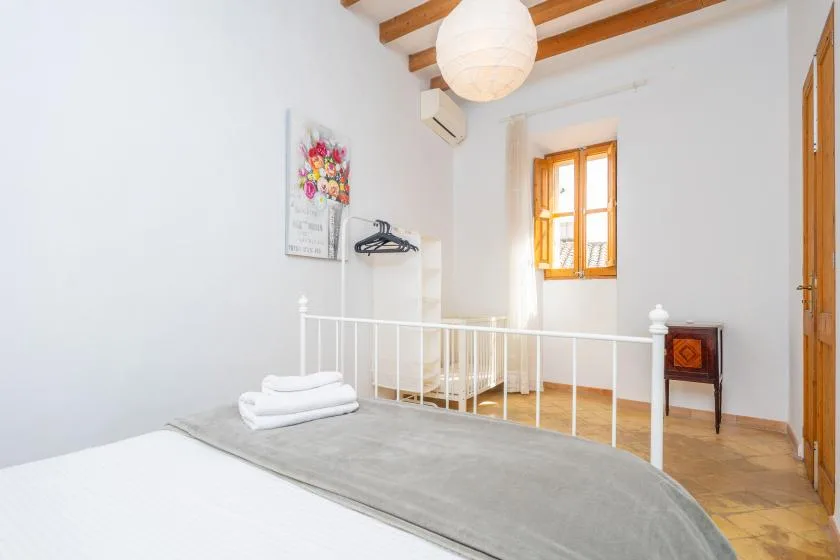 A bright bedroom with a bed, white railing, and a sunlit window.