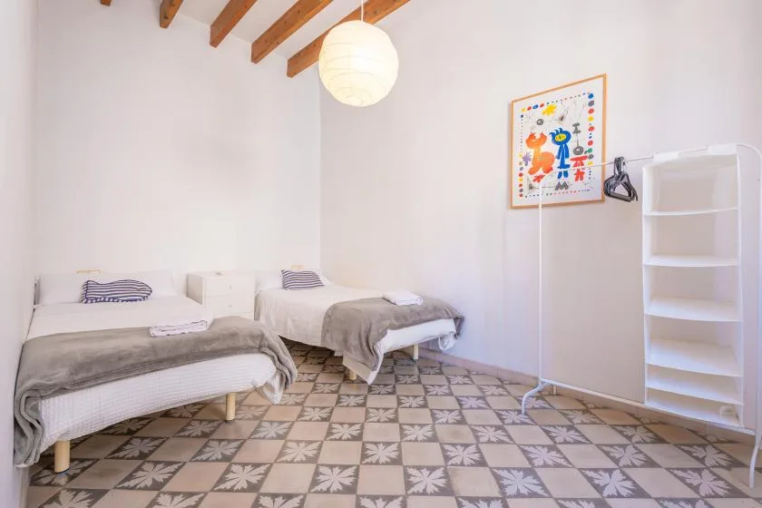 A bright bedroom with two single beds, exposed ceiling beams, and patterned floor tiles.