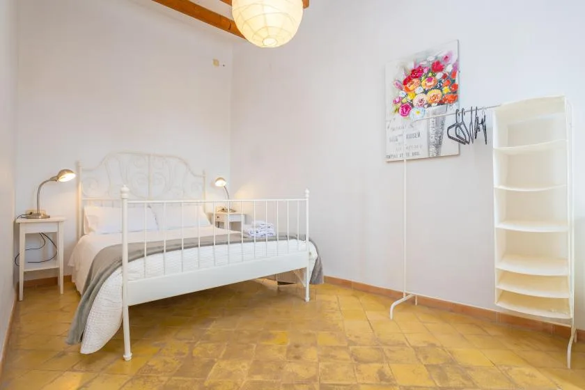 A bedroom with a white bed, bedside tables, and a freestanding shelf.