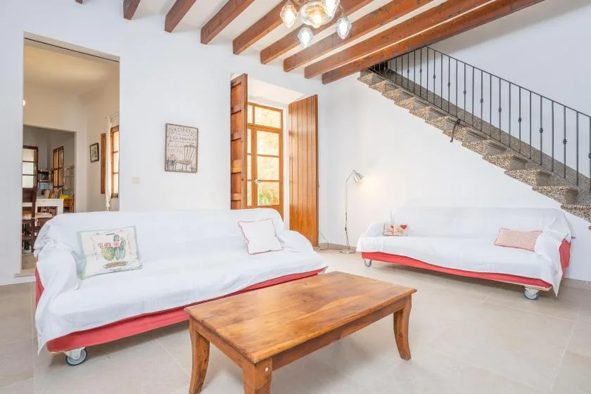 A bright living room with white seating, a wooden coffee table, and a staircase.