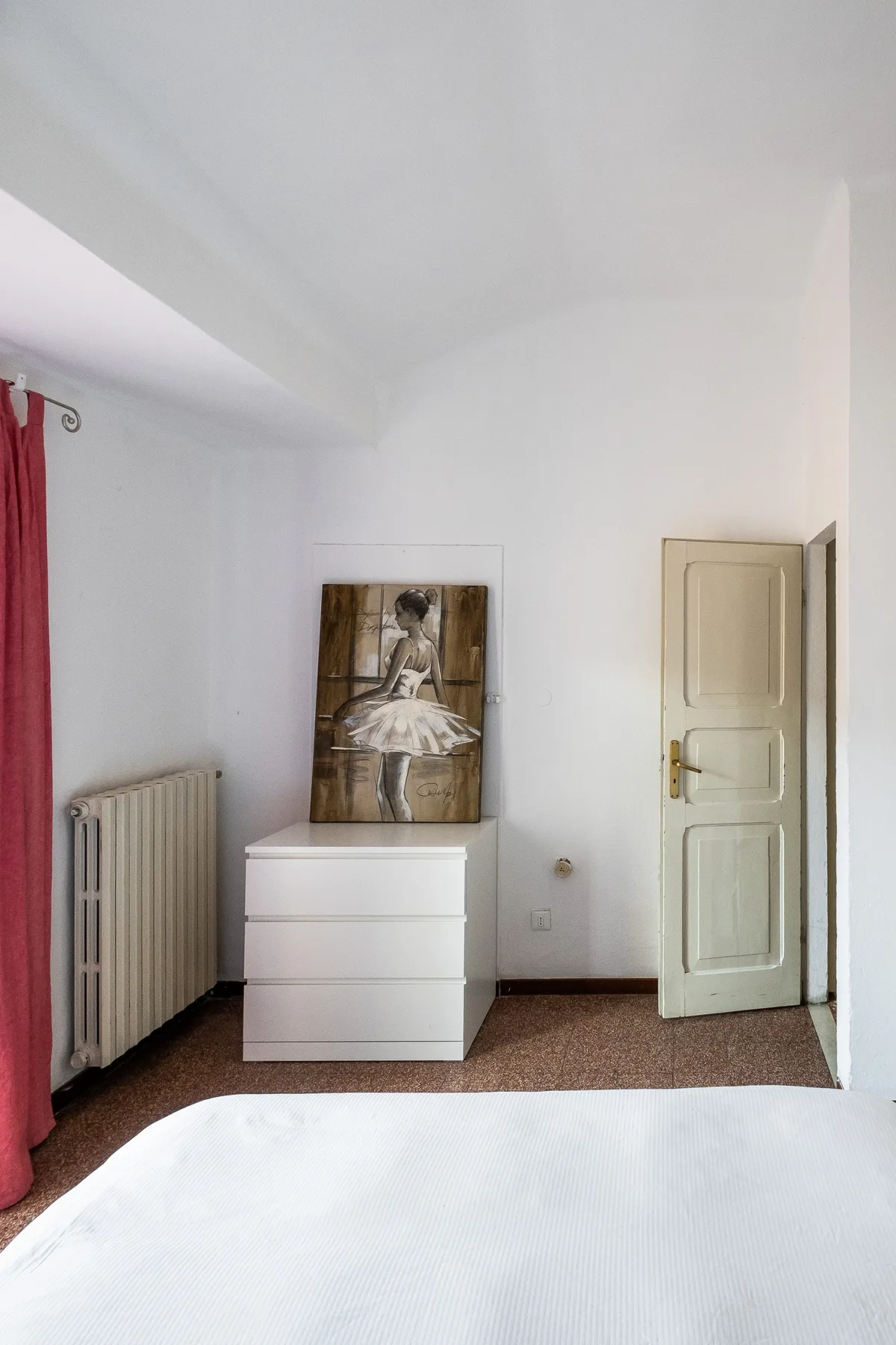 A bedroom with a bed, a dresser, and framed artwork leaning against the wall.