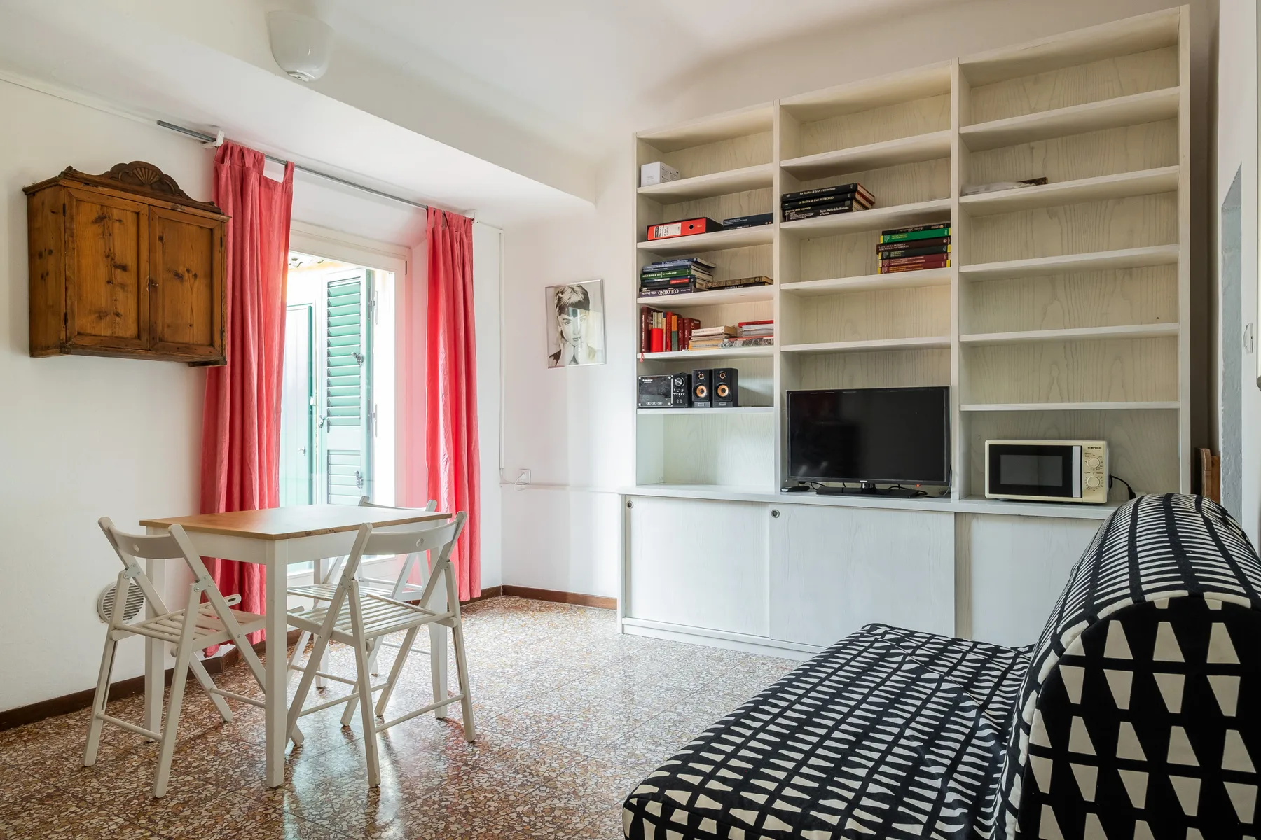 Una sala luminosa con estanterías empotradas, un televisor y una pequeña mesa de comedor.