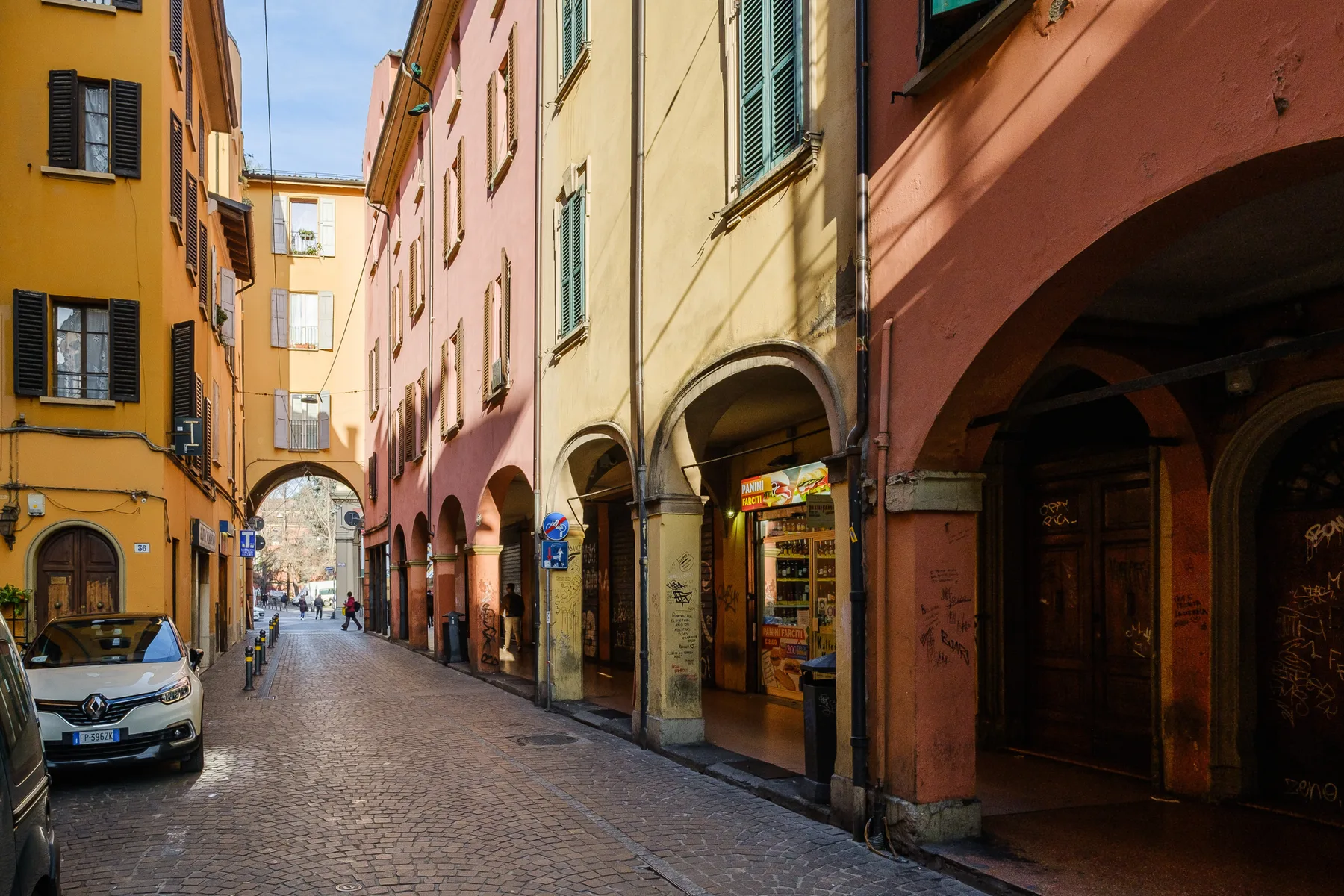 A cobblestone street runs between colorful buildings with arched storefronts.