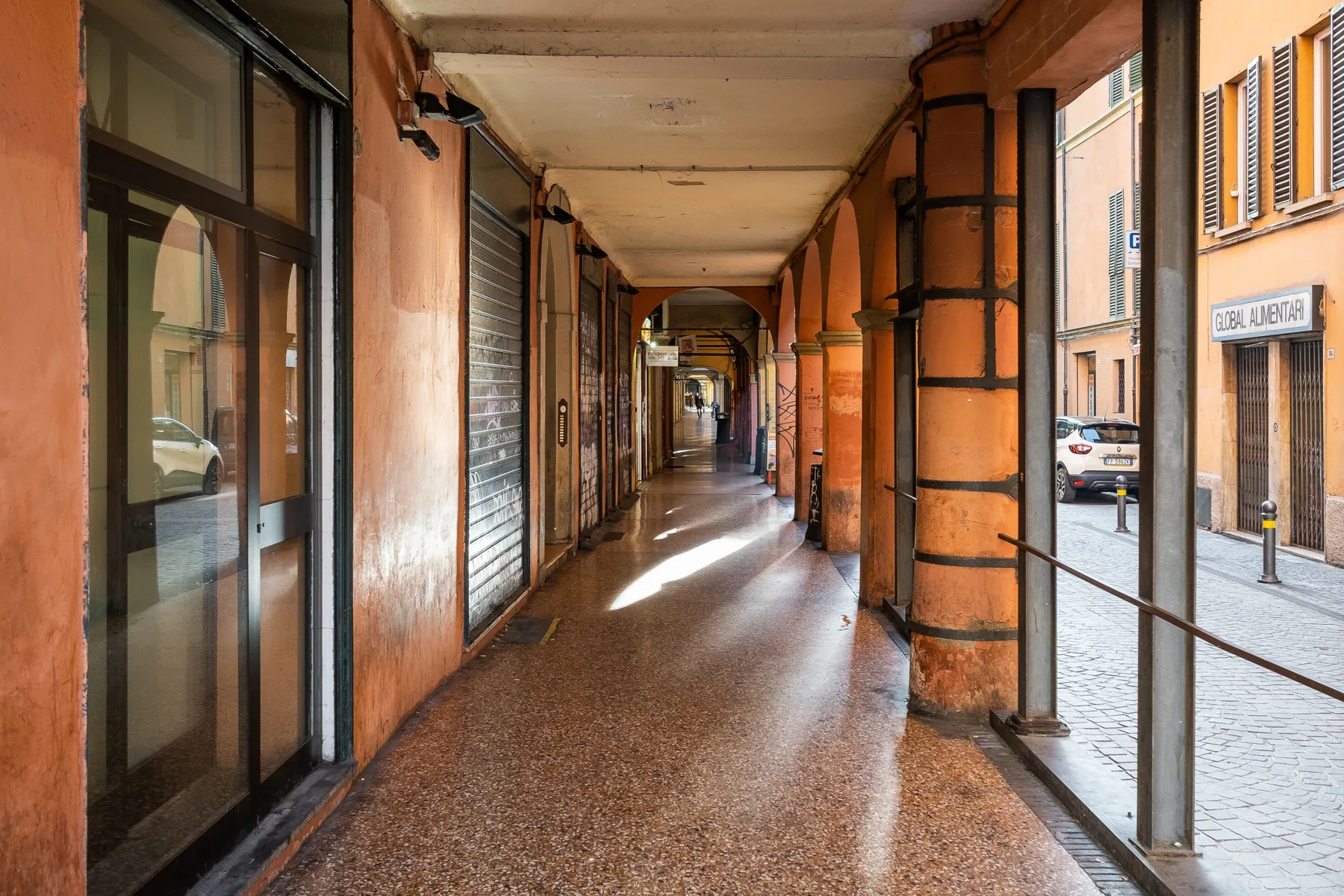 A covered walkway with orange columns and storefronts.