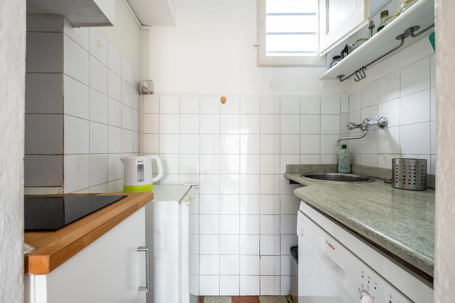 A compact kitchen with tiled walls, countertops, and white cabinets.