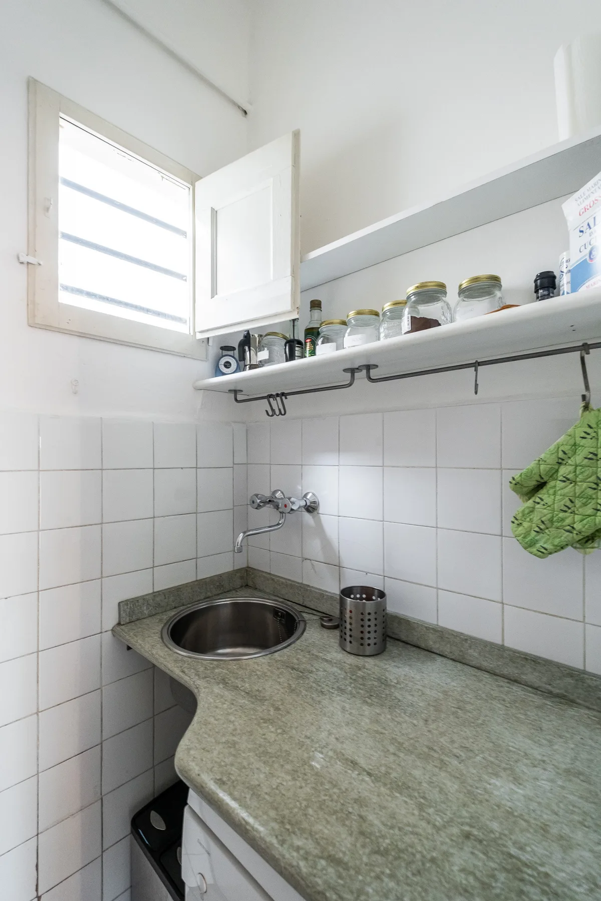 A compact kitchen counter with a sink and open shelves holding jars.