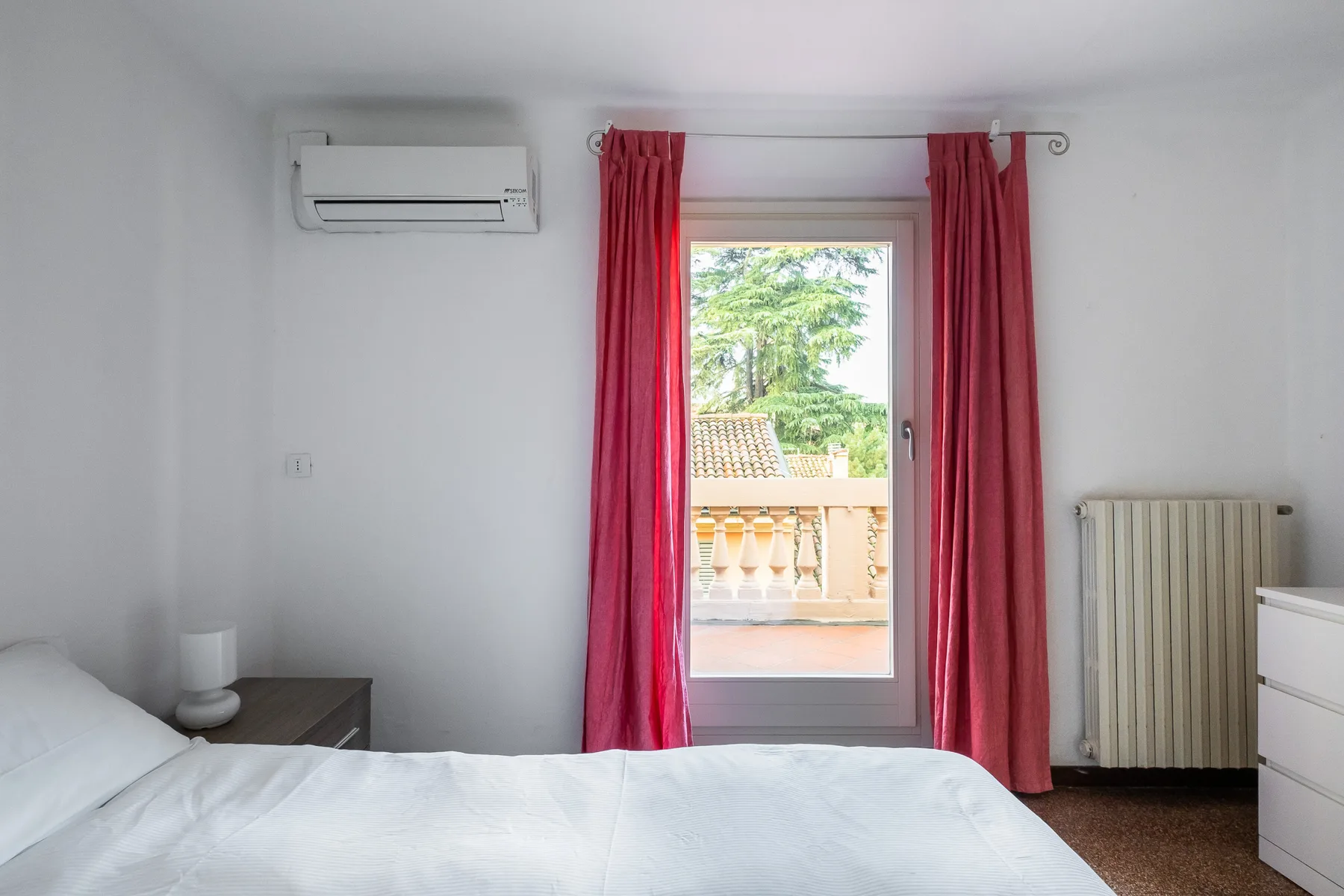 Un dormitorio con una cama frente a una puerta de vidrio enmarcada por cortinas rojas.