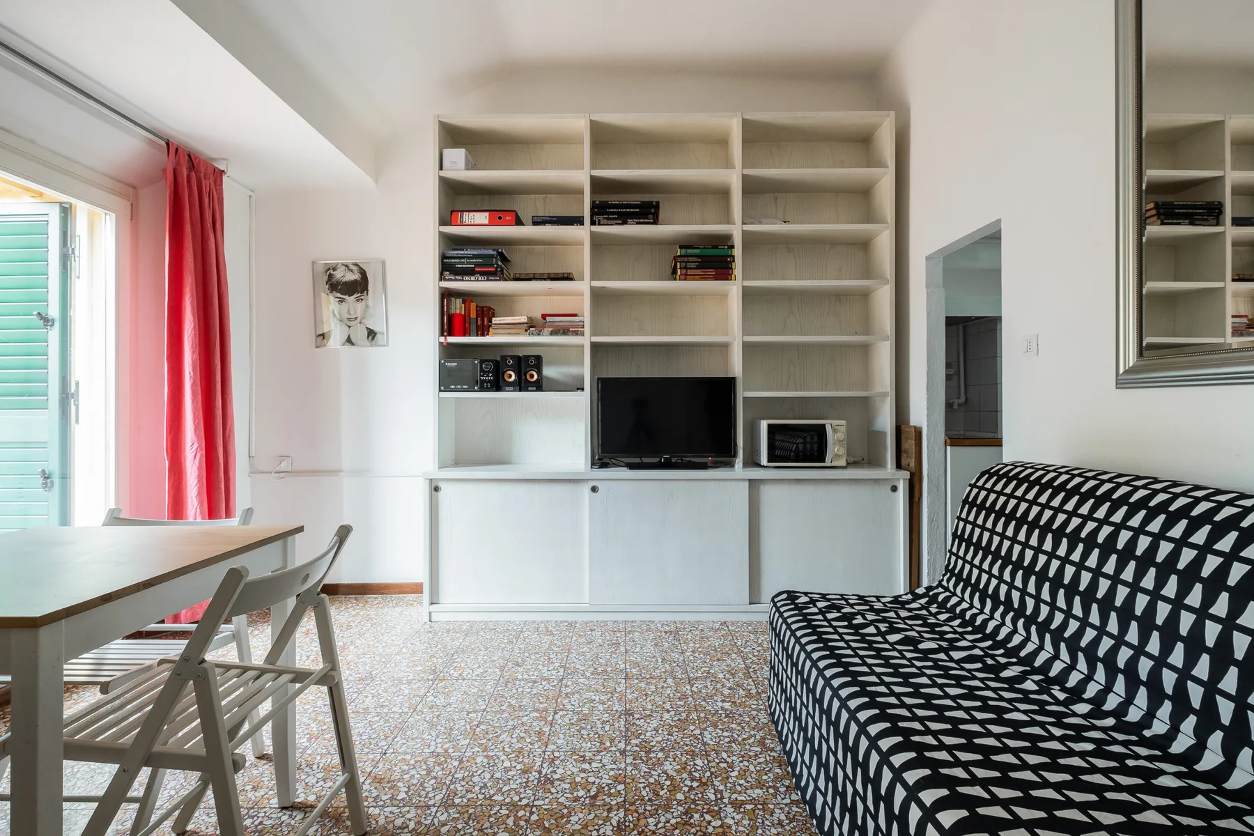 A bright living room with built-in shelving, a television, and patterned seating.