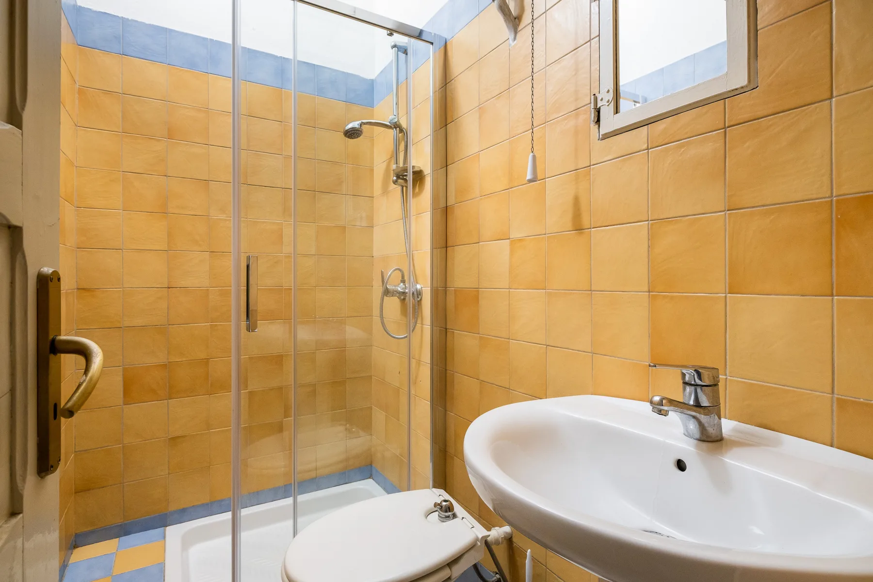 A tiled bathroom with a glass shower, toilet, and sink.