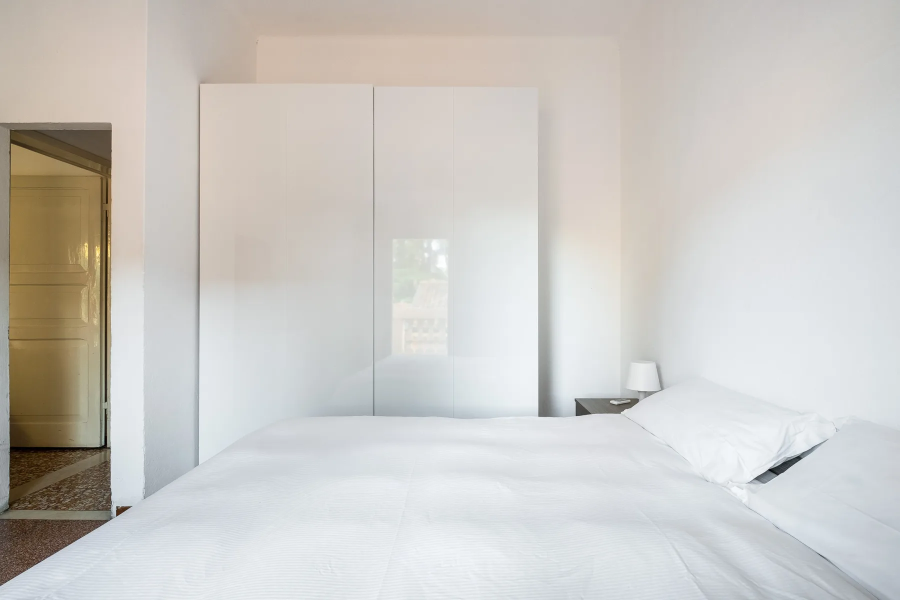 A bright bedroom with white bedding and a tall white wardrobe.