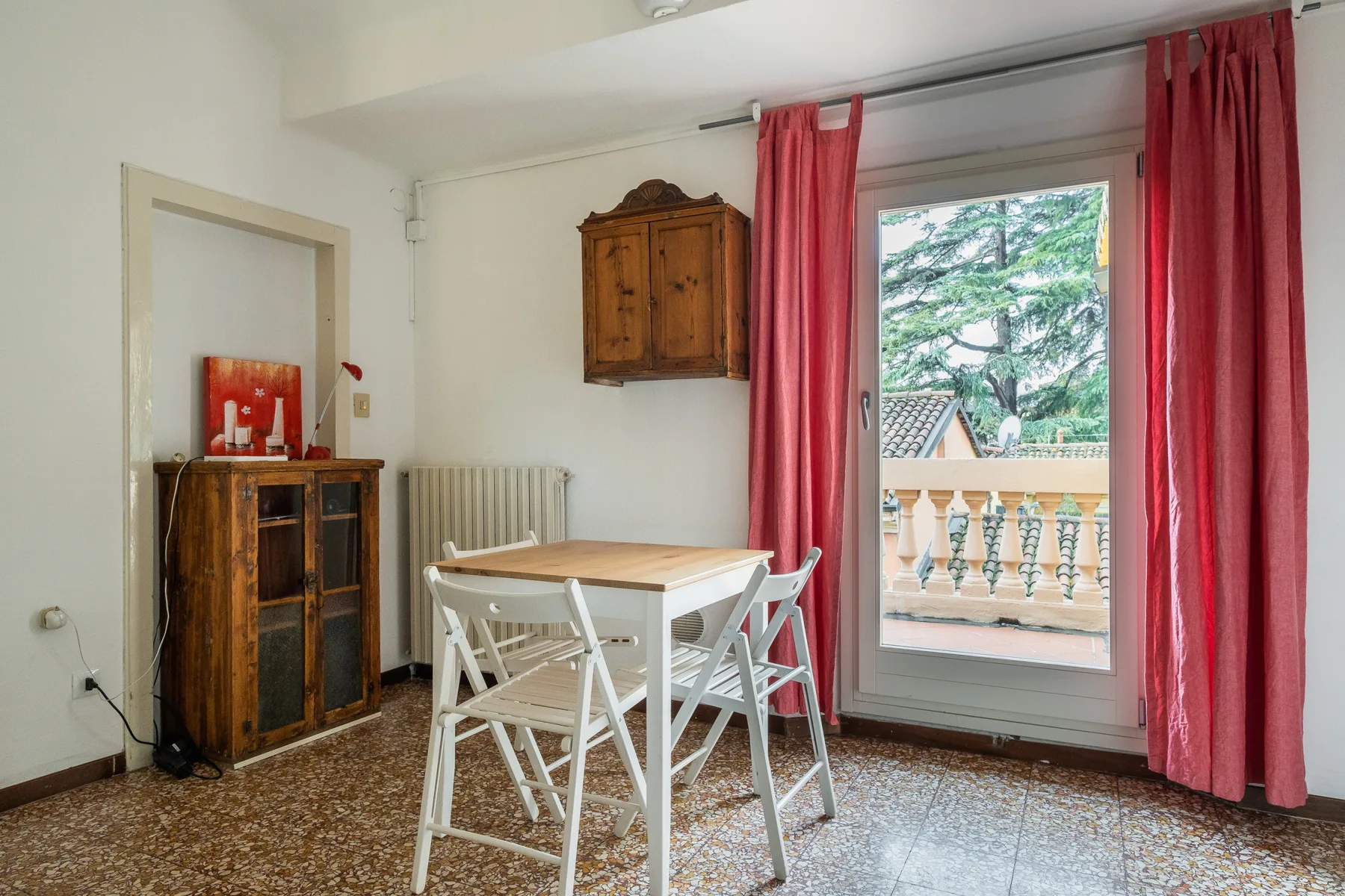 A dining area with a white table and chairs beside a glass door opening onto a balcony.
