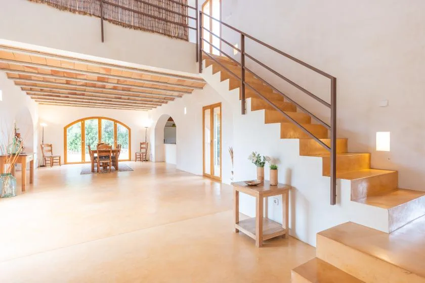 A bright open interior with a wooden staircase and a dining area at the back.