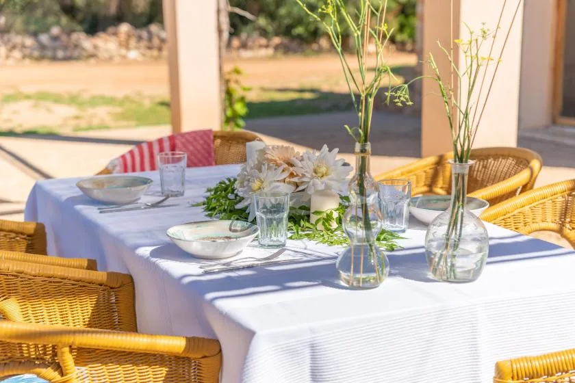 A set dining table on a patio with woven seating and floral centerpieces.