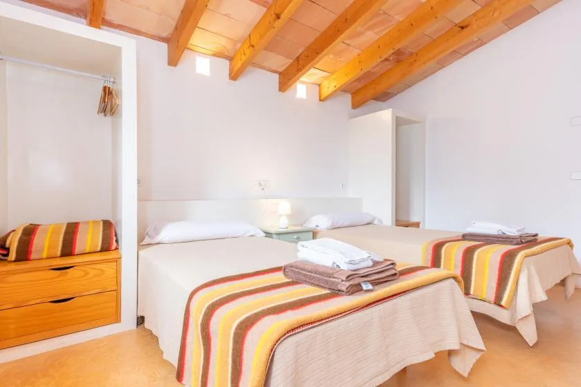 A bright bedroom with two beds, striped blankets, and exposed wooden ceiling beams.