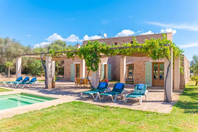 A stone house with a vine-covered patio beside a swimming pool.