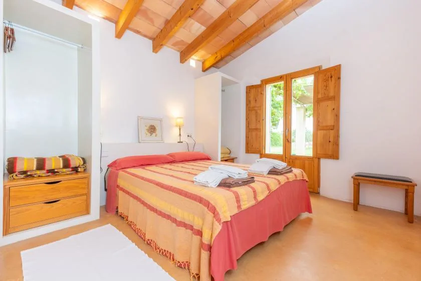 A bedroom with a bed, wooden ceiling beams, and an open window.