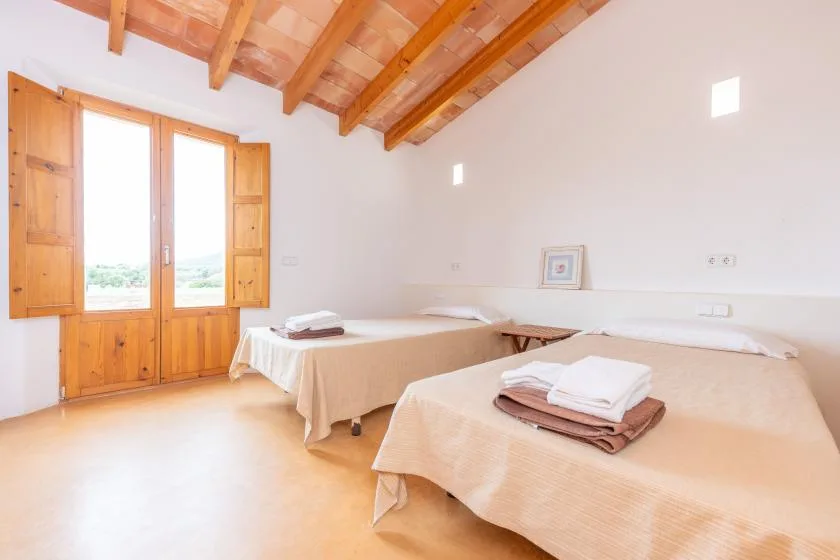 A bright bedroom with two beds and an open wooden-shuttered window.
