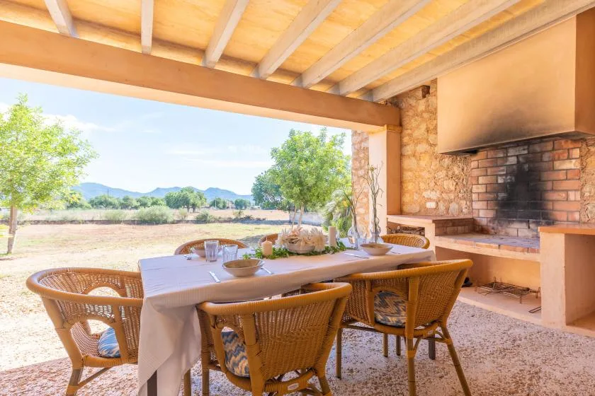 A covered outdoor dining area with a long table and a built-in brick barbecue.