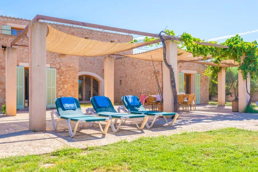 A stone courtyard with lounge seating beneath a vine-covered pergola.