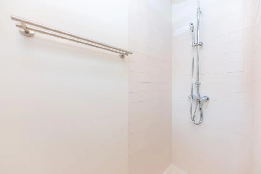 A tiled bathroom wall with a mounted shower and grab bar.