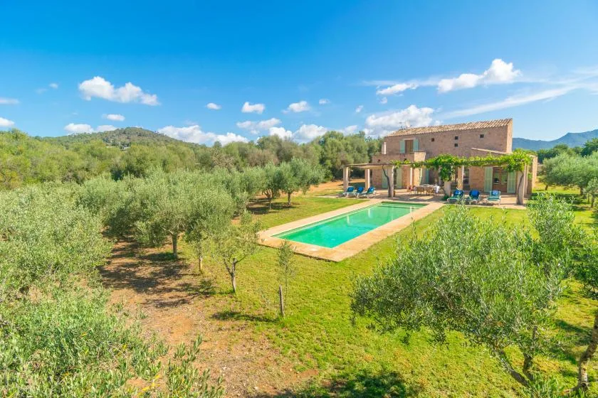A countryside house stands beside a swimming pool, surrounded by trees and greenery.