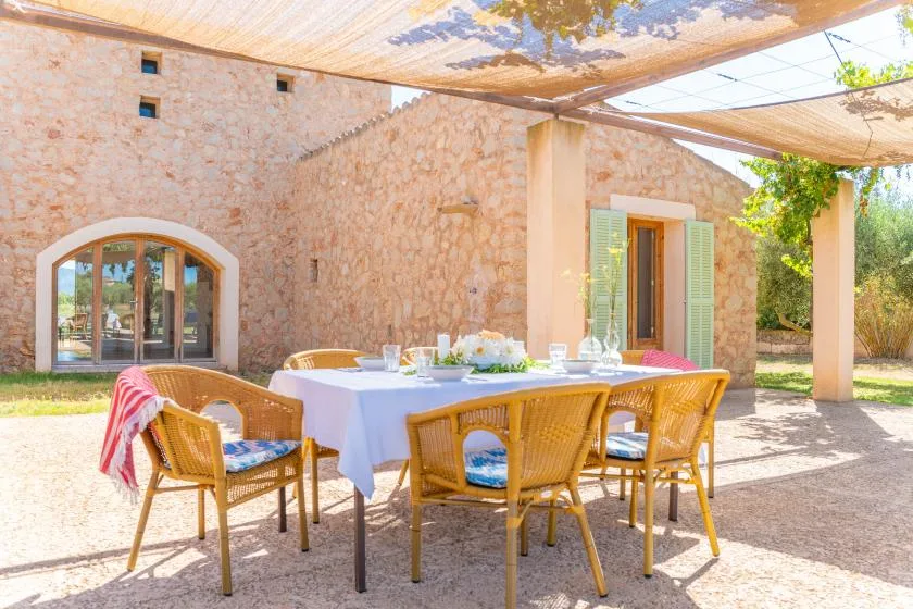 A shaded outdoor dining area with a table set beside a stone building.