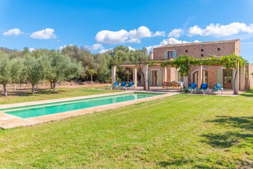 A house and outdoor swimming pool sit in a grassy yard with trees.