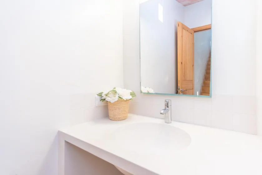 A bright bathroom vanity with a sink, mirror, and small flower arrangement.