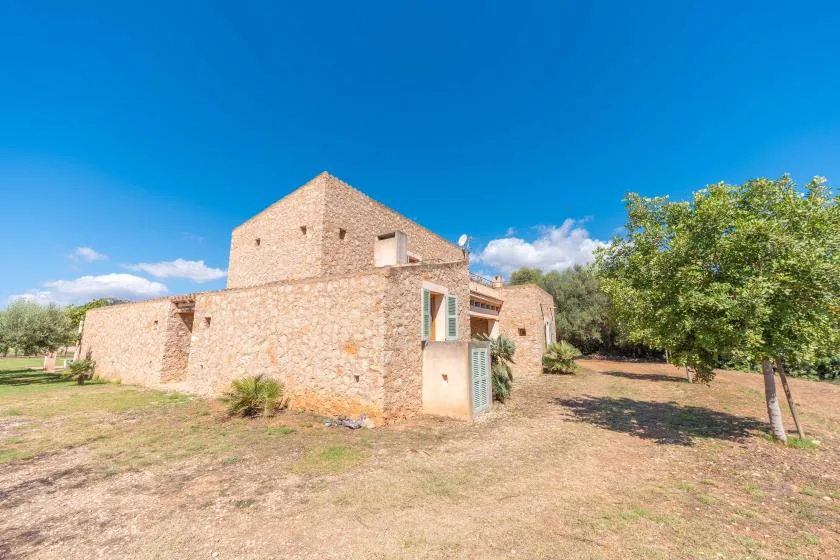 A stone house stands in a dry yard beneath a clear blue sky.