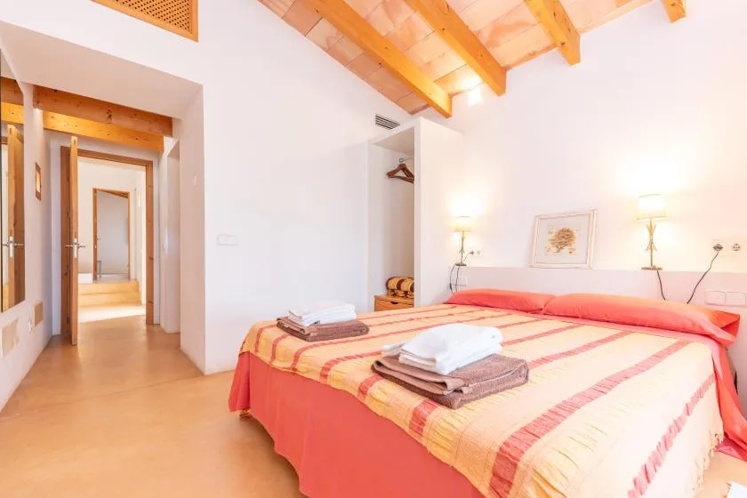 A bedroom with a bed dressed in striped bedding and exposed wooden ceiling beams.
