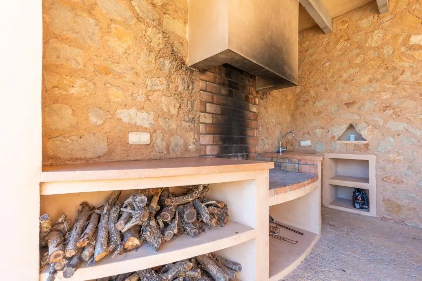 A rustic stone barbecue area with a built-in grill and stacked firewood.