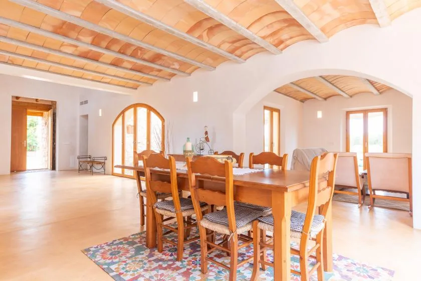 A bright dining room with a long wooden table and chairs beneath a beamed ceiling.