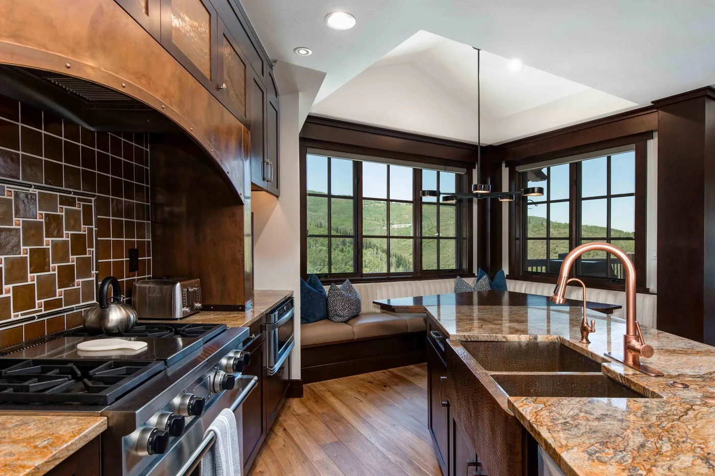 A kitchen with a large island and broad windows overlooking a green landscape.
