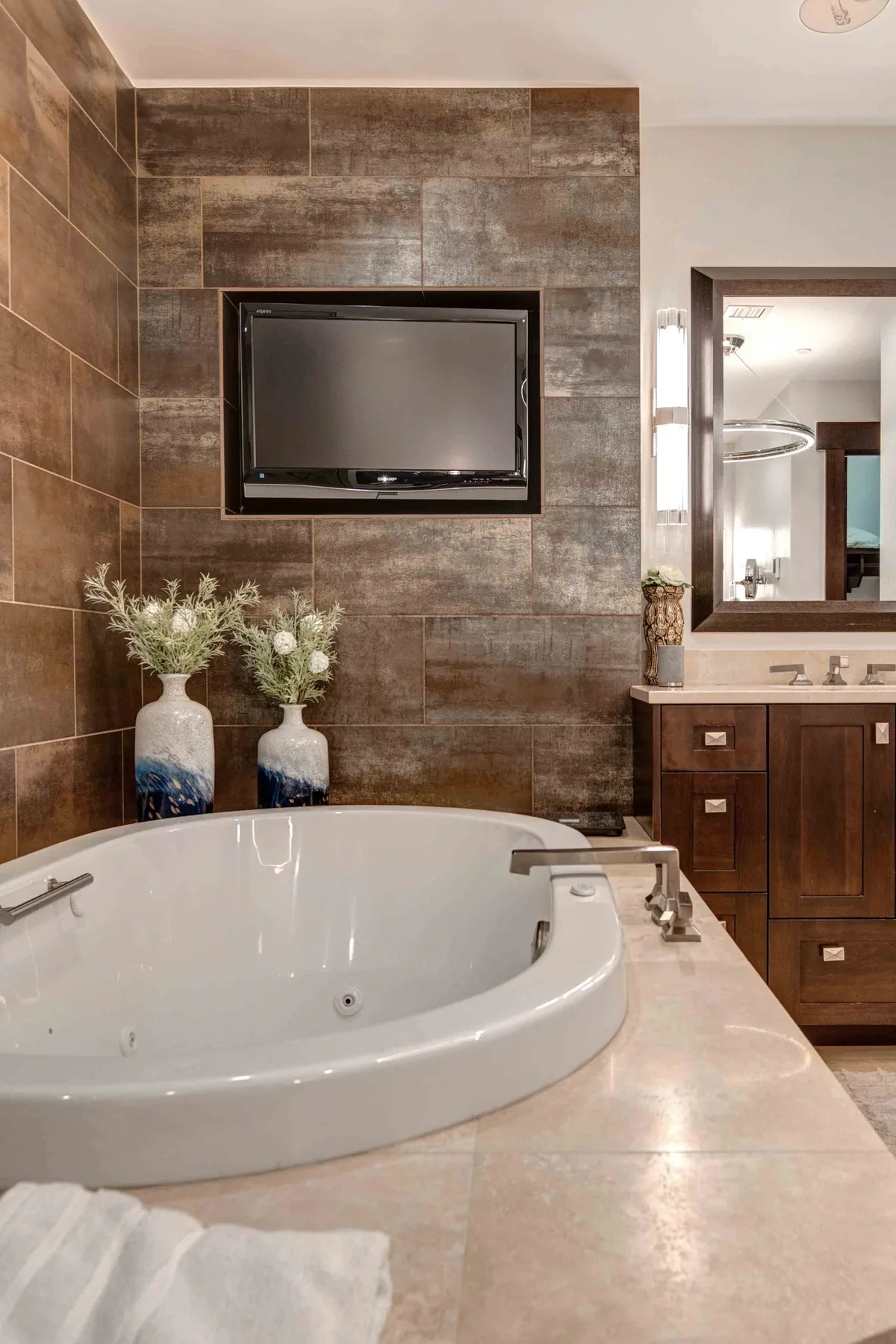 A bathroom with a large bathtub, wall-mounted television, and vanity.