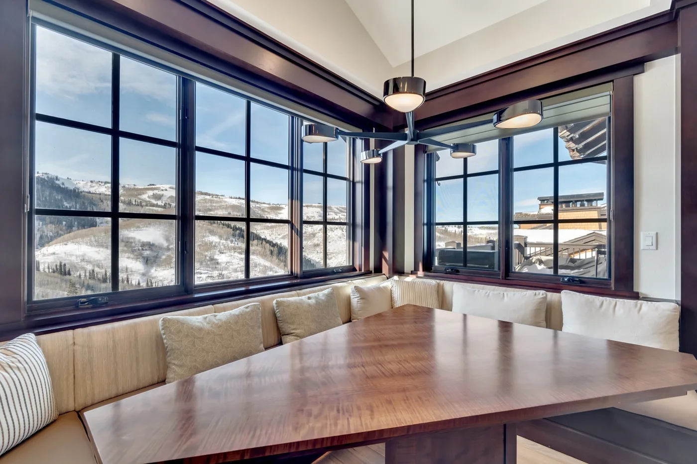 A dining nook with a wooden table and corner windows overlooking a snowy landscape.
