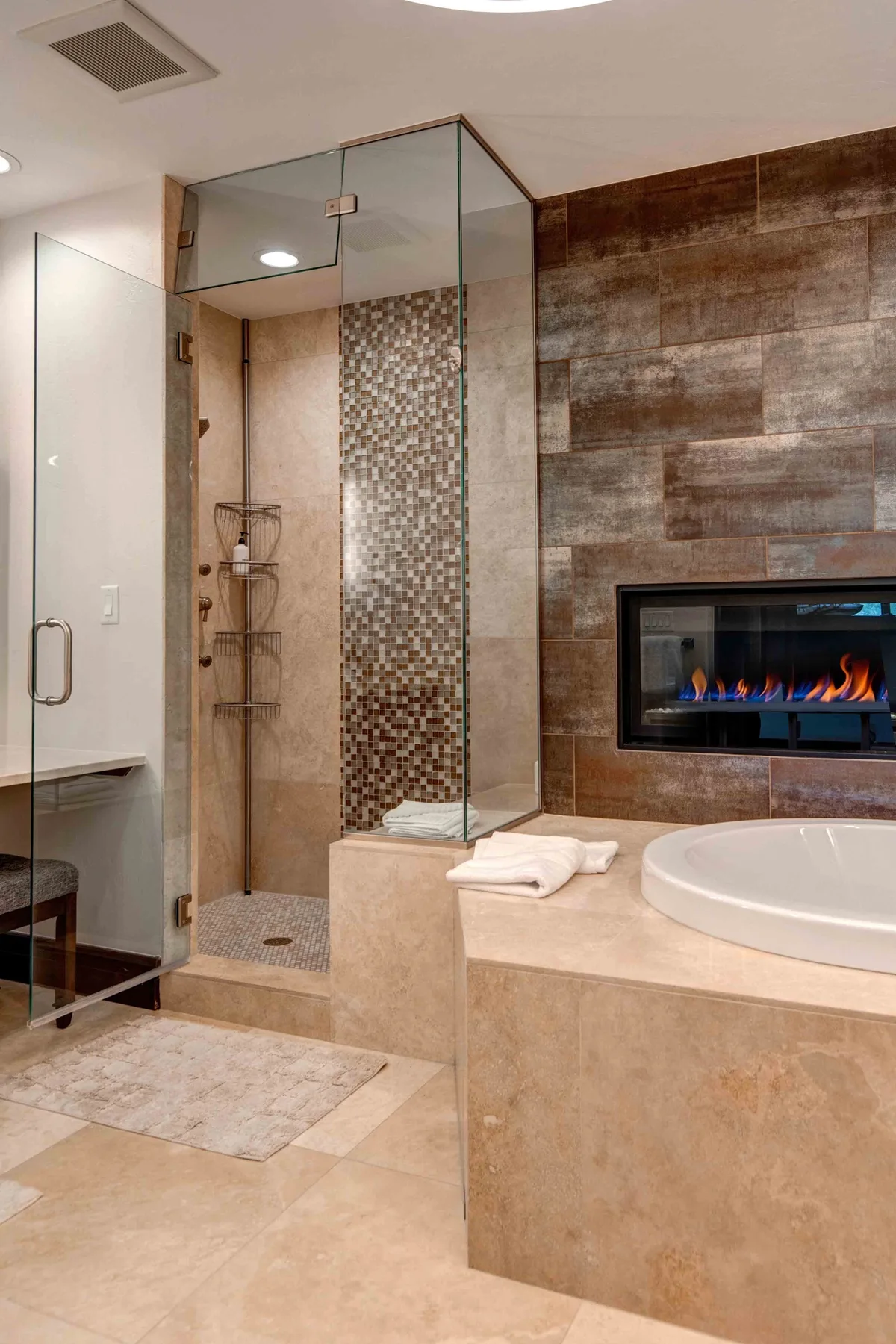 A modern bathroom with a glass shower and a built-in fireplace.