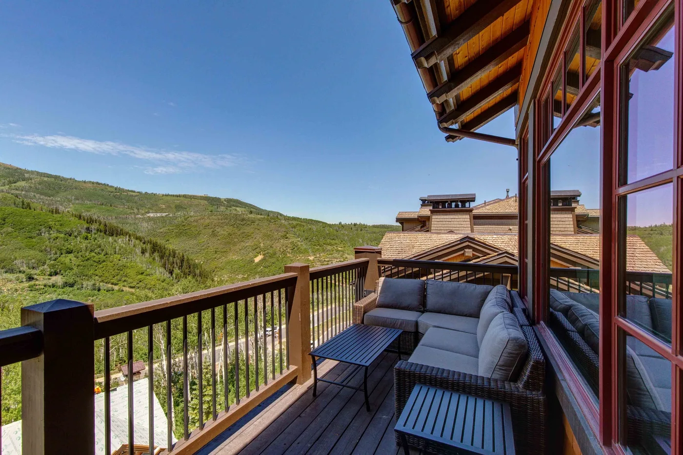 A balcony seating area overlooks green hills beneath a clear blue sky.