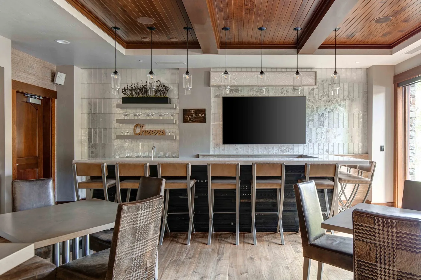 A dining area with a long table, bar seating, and a wall-mounted television.