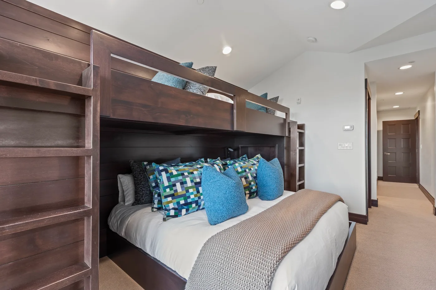 A bedroom with a bed framed by built-in wooden shelving and colorful pillows.