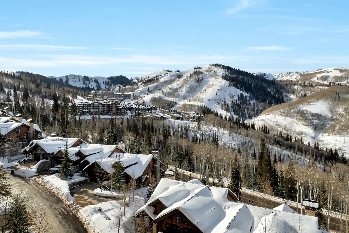 Snow-covered buildings sit below wooded hills and snowy mountain slopes.