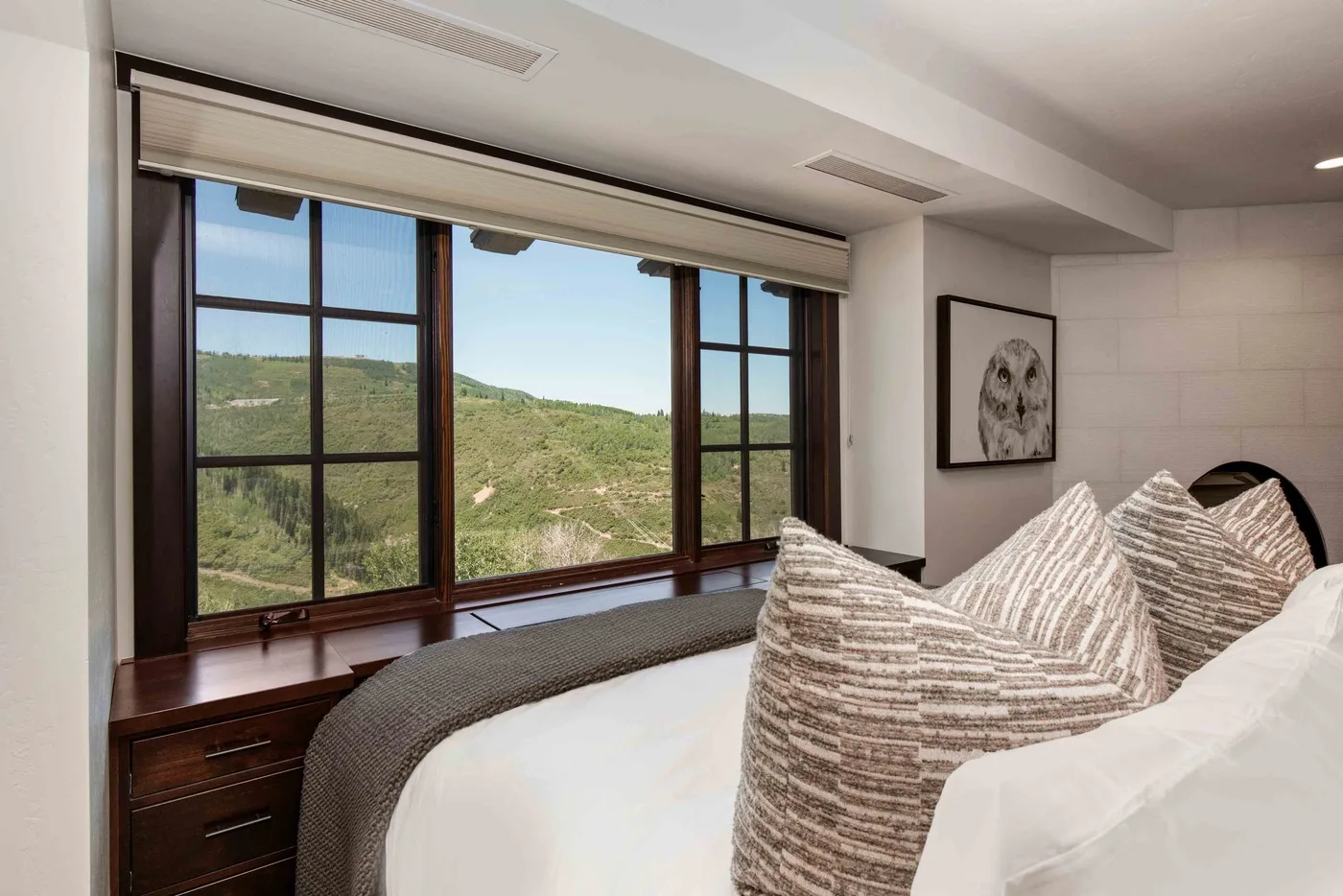 A bedroom with a bed beside large windows overlooking green hills.