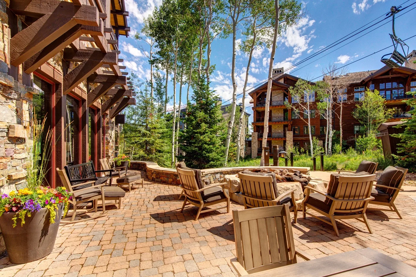 A paved outdoor seating area with wooden chairs and tables beside trees.