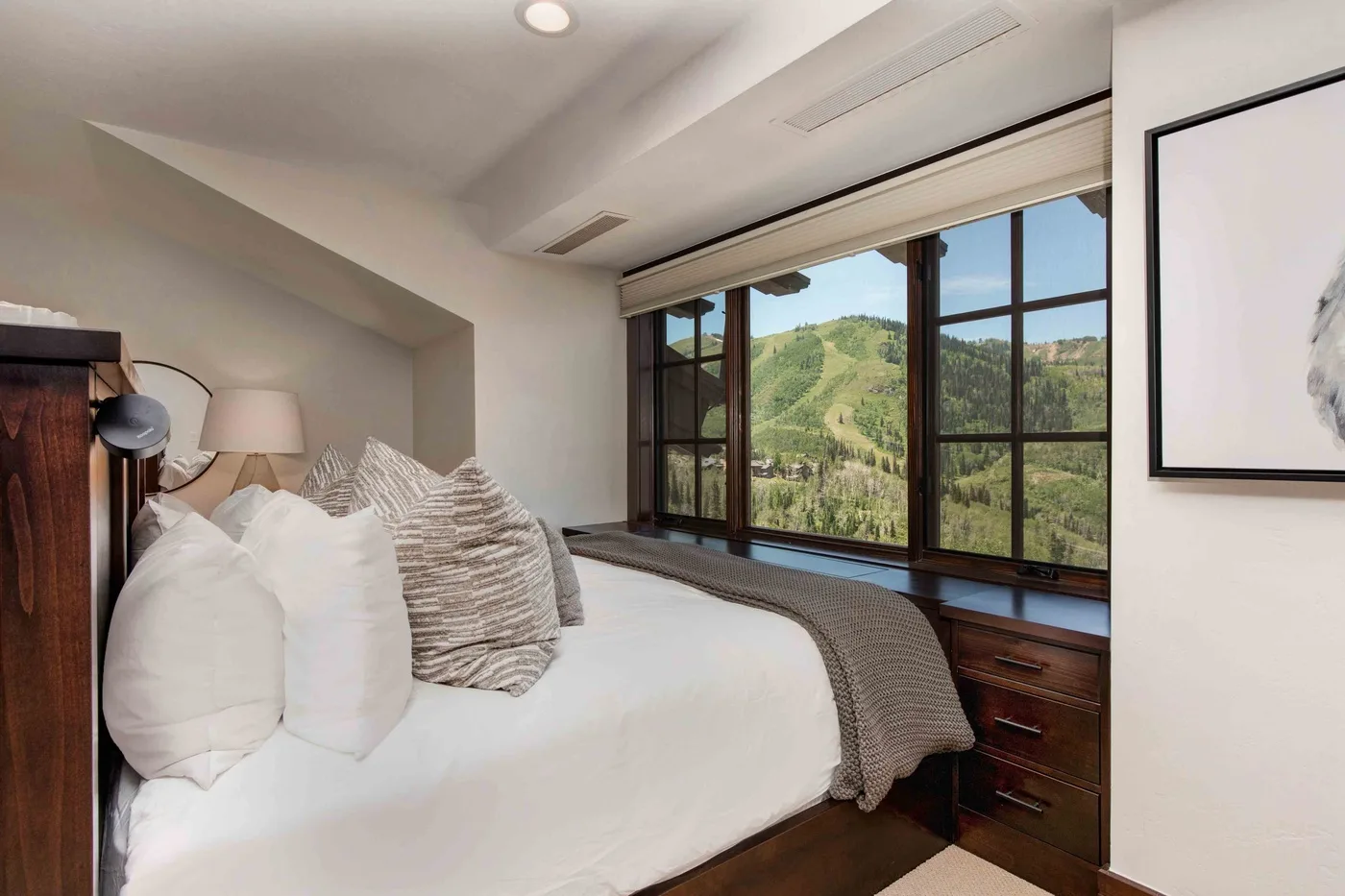 A bedroom with a bed beside large windows overlooking green hills.