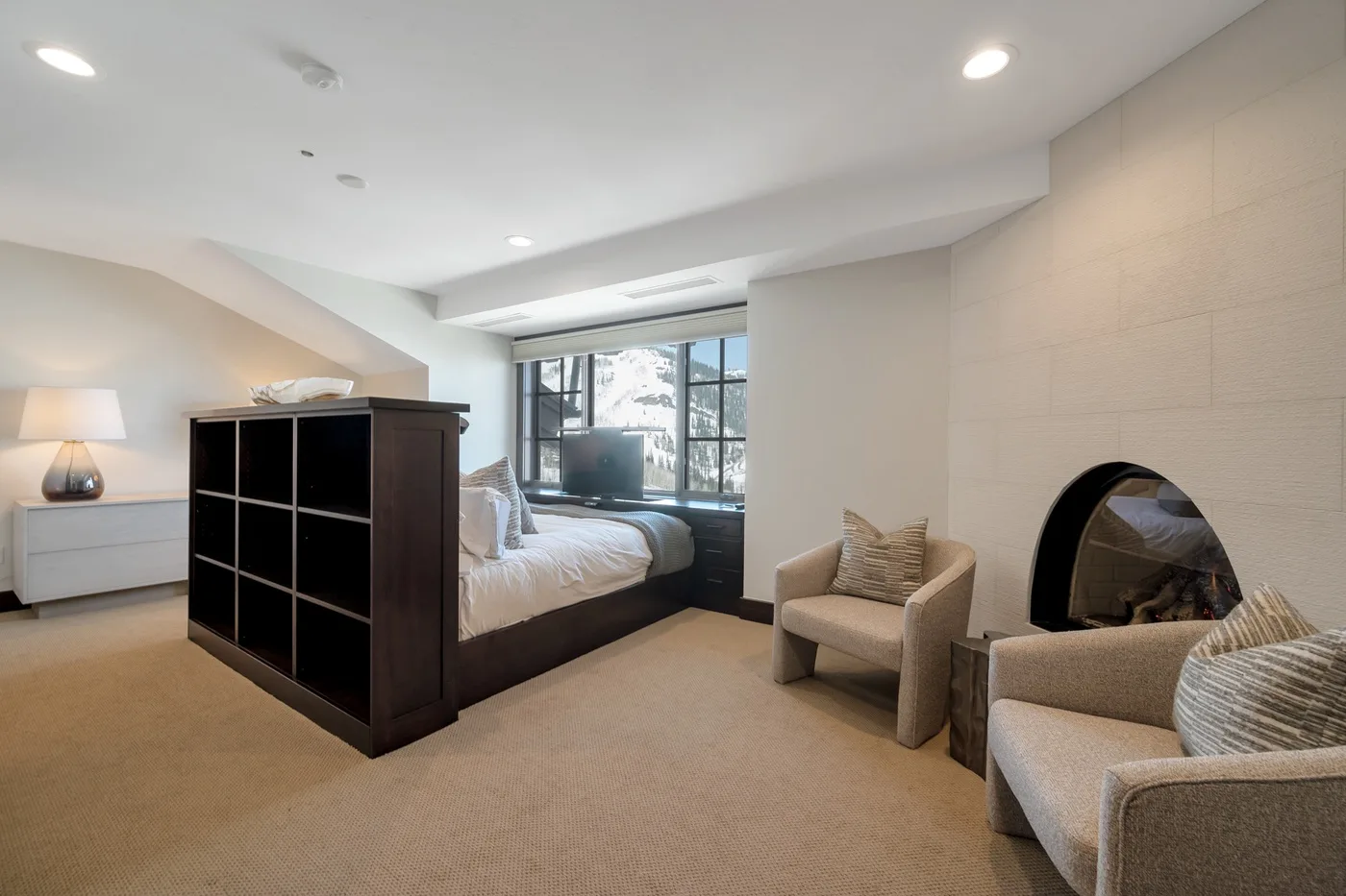 A bedroom with a bed, a pair of armchairs, and a fireplace.