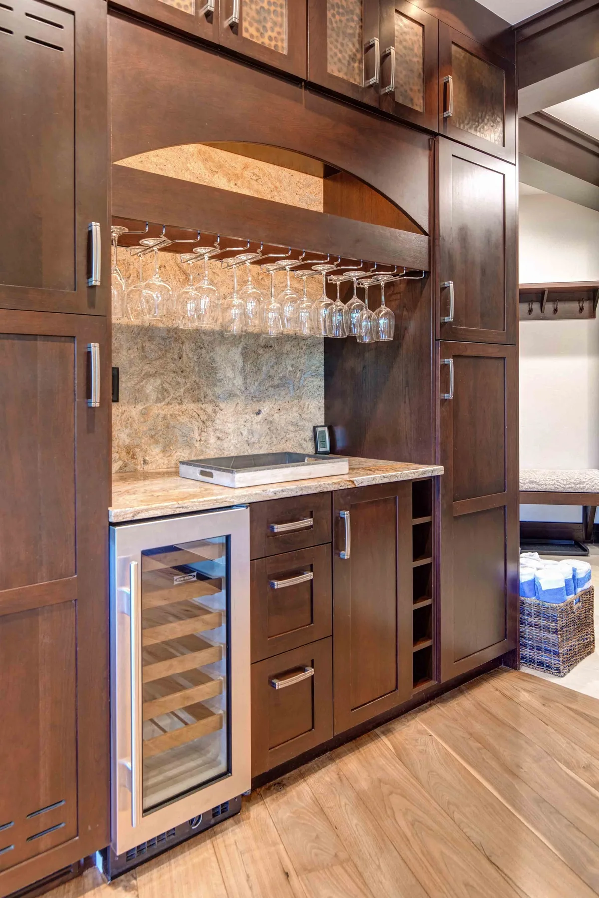 A built-in bar area with glassware above a counter and a compact beverage refrigerator.