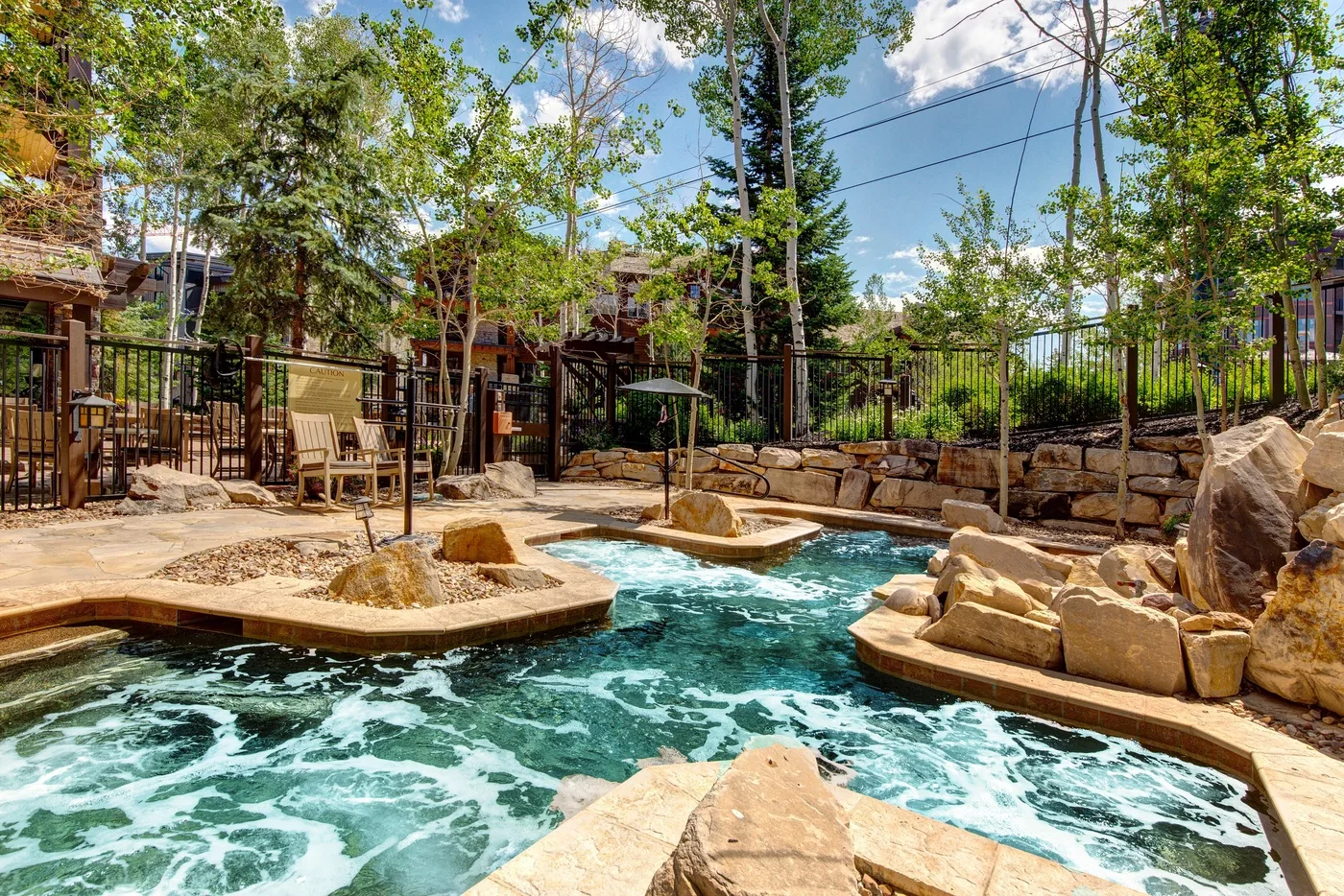 A landscaped outdoor pool with flowing water, stone features, and surrounding trees.