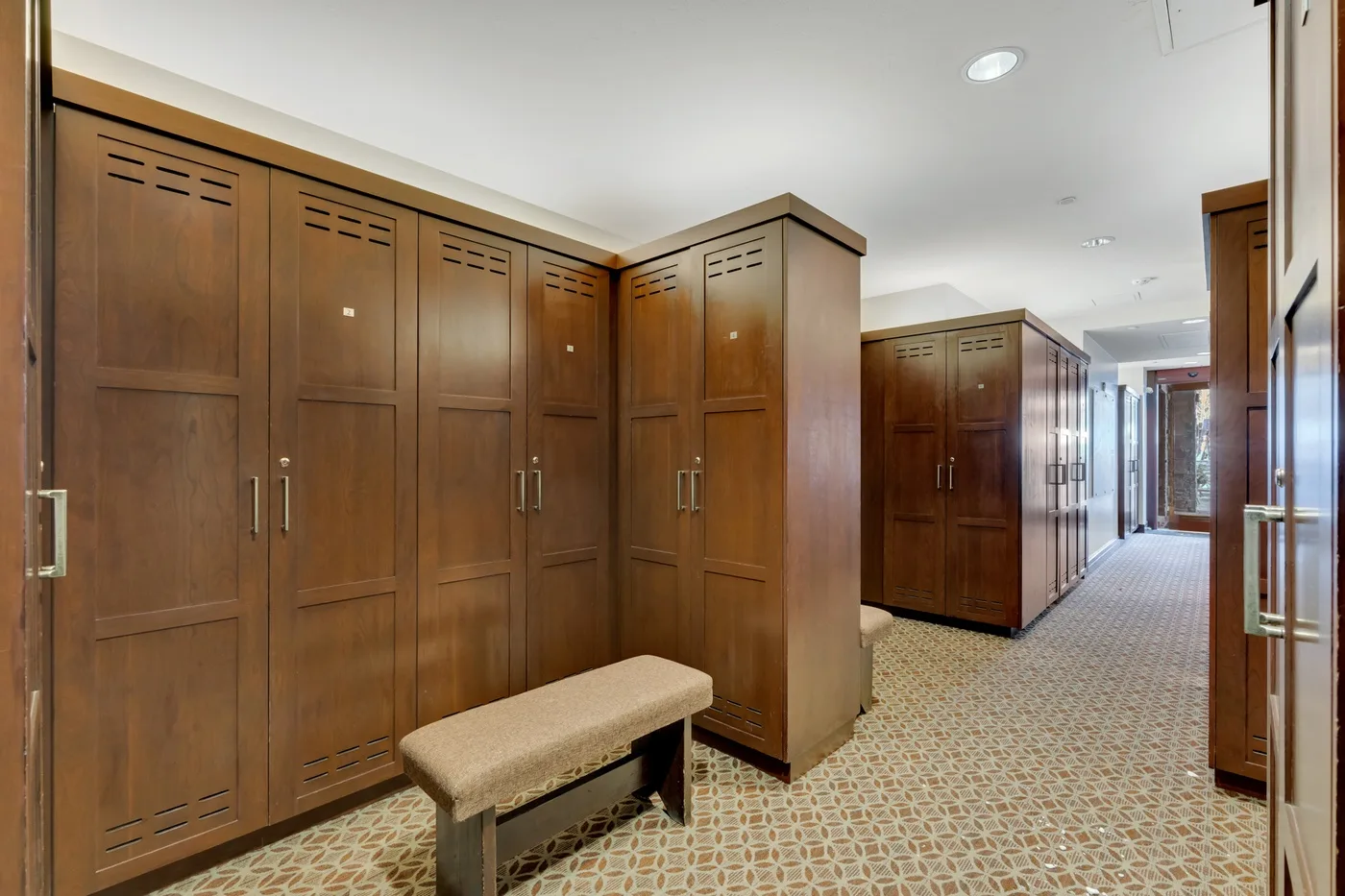 A locker room with rows of wooden lockers and a cushioned bench.