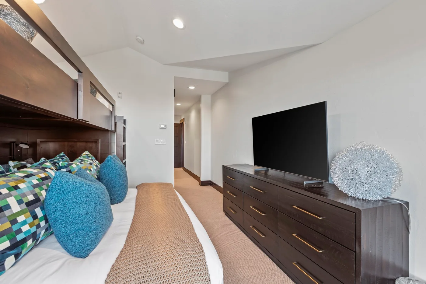 A bedroom with a bed beside a dresser and a large television.