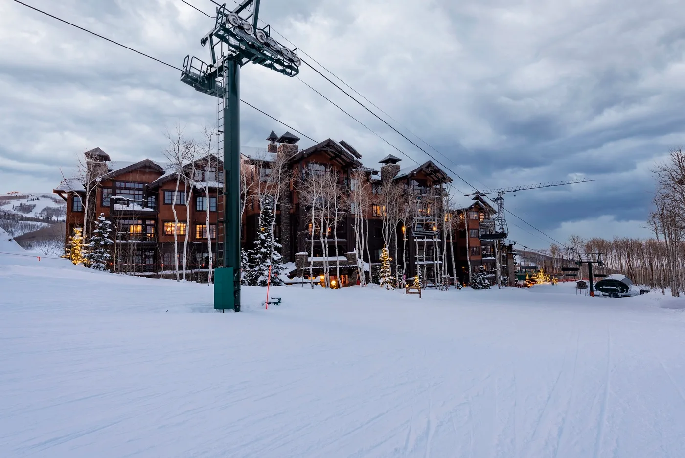 Snow-covered ski slope beside a large lodge, with ski-lift cables overhead.